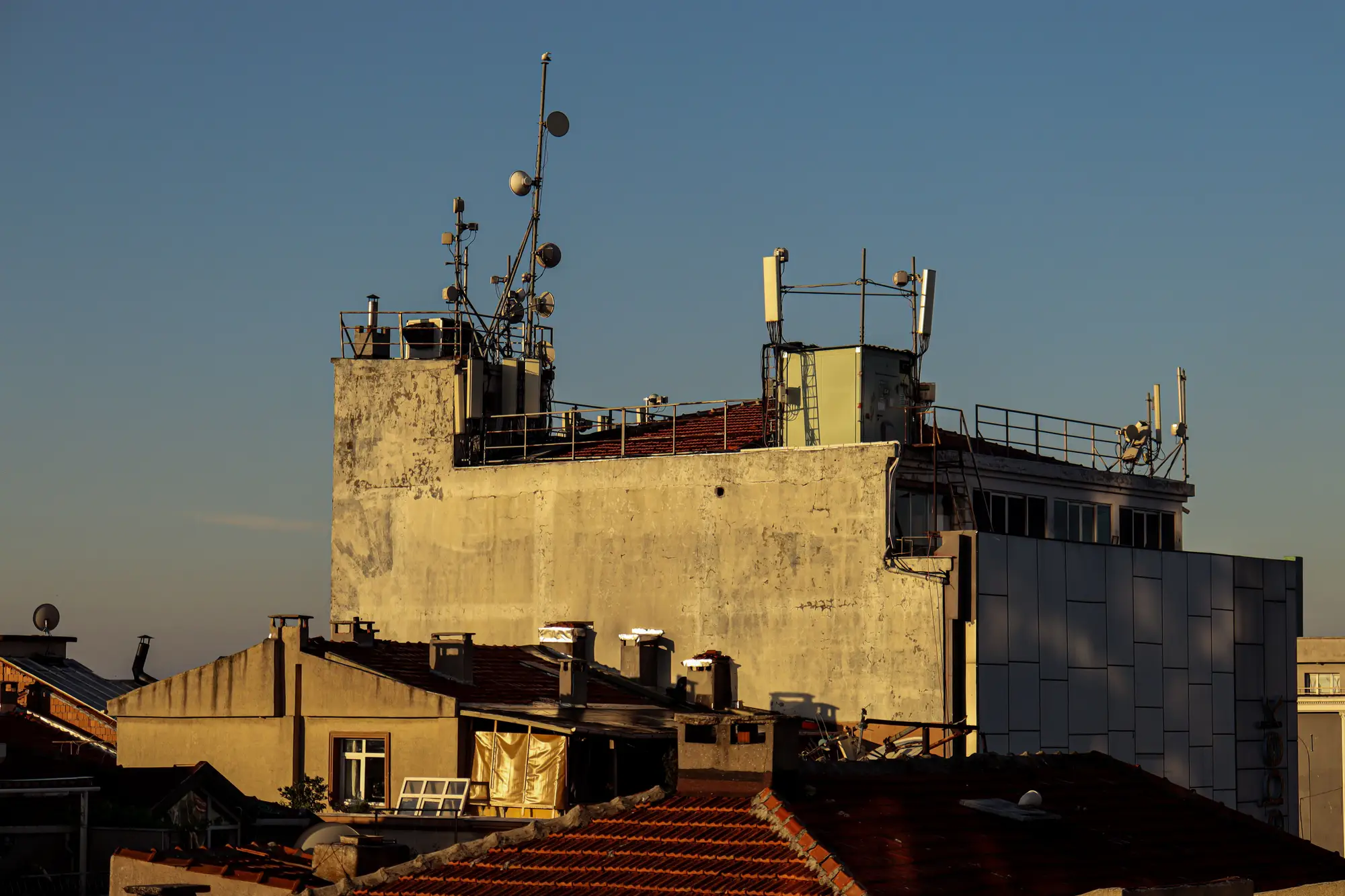 Antenna masts on a city rooftop above tiled roofs at sunset